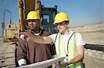 Bauarbeiter Schutzhelme tragen, steht vor der schweren Ausrüstung, Blick auf den plan