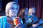 Young woman drinking soft drink, sitting with Friends, Watching Movie in theatre