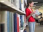 Teenage student reading text books by library shelf