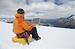 Hiker using laptop on snowy mountain peak, back view