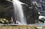 Hikers standing under waterfall at river