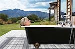 Woman taking bath on porch by mountains