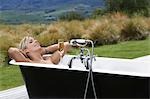 Woman taking bath with champagne on porch in countryside