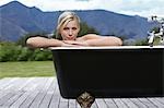 Woman in bathtub on porch by mountains