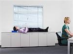 Homme d'affaires de dormir sur les armoires de bureau près de femme travaillant
