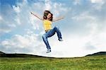 Woman jumping for joy in mountain meadow, front view