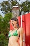 Screaming young woman using outdoor shower, low angle view