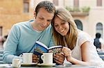 Couple at outdoor cafe looking at guidebook of Rome, front view
