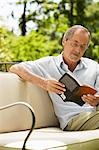 Man sitting on sofa in back yard reading book