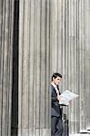 Businessman standing outside building between pillars reading newspaper