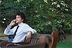 Businessman sitting on park bench talking on cell phone