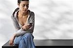 Young woman sitting indoors on bench ending text message