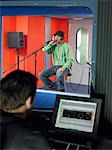 Young man singing in studio, technician in foreground