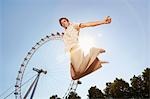 Young man in park jumping in front of London Eye, portrait, low angle view