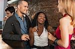 Couple with friend holding drinks laughing, standing at bar