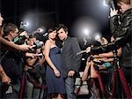 Couple posing on red carpet, being photographed by paparazzi