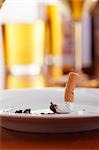 Cigarette in ashtray on table with glasses of beer
