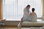 Doctor using stethoscope on back of patient in hospital room, back view of patient