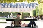 Young couple reading book, sitting on bench in park