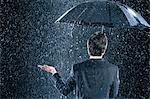 Businessman staying dry under umbrella during downpour, back view