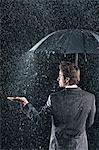 Businessman sticking hand out from under umbrella to feel rain, back view