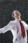 Businessman standing, arms spread facing incoming rain