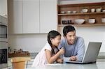 Father and daughter playing with laptop on kitchen counter