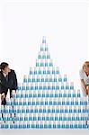 Homme et femme admirant pyramide des gobelets en plastique empilés sur fond blanc