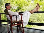 Adult man in bathrobe, sitting on chair at terrace with feet up
