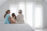 Grandmother, mother and daughter sitting on bed in bedroom