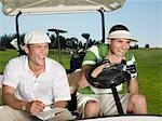 Two young male golfers sitting in cart, laughing