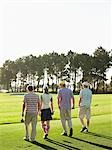 Vier junge Golfer gehen auf Kurs, Rückansicht