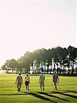 Four young golfers walking on course, back view