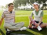 Deux jeunes golfeurs assis sur cour, souriant