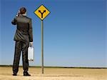 Rear view of confused businessman looking at desert road sign