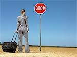 Business woman with luggage, standing in front of stop sign in desert, back view