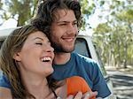 Young couple embracing, leaning against front of van parked by road, head and shoulders