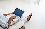 Man using laptop, sitting on sofa in living room, low section, elevated view