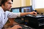 Man using computer keyboard and adjusting knob on mixer.