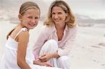 Mother and daughter (7-9) sitting on beach, portrait