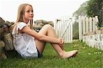 Girl (10-12) sitting against wall in garden
