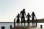 Trois enfants (7-9) main dans la main avec le père, debout sur le bord du quai, vue postérieure.