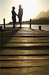Couple standing on dock by lake, holding hands, side view.