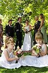 Two young girls sitting on lawn, holding bouquets, bride and groom in background