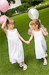 Two young girls walking in garden, holding balloons