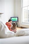 Mother and daughter (5-6) watching cartoons in television, back view