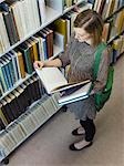 Young woman looking through book in library, view from above