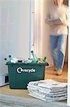 Recycling container and pile of waste paper on floor, woman walking in background (motion blur)