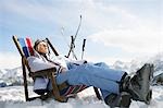 Female skier resting on deckchair in mountains