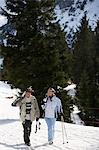 Skiing couple walking, carrying skis on shoulders, on ski slope